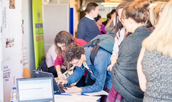 Students using a laptop at a busy recruitment fair, ϲ campus, Edinburgh