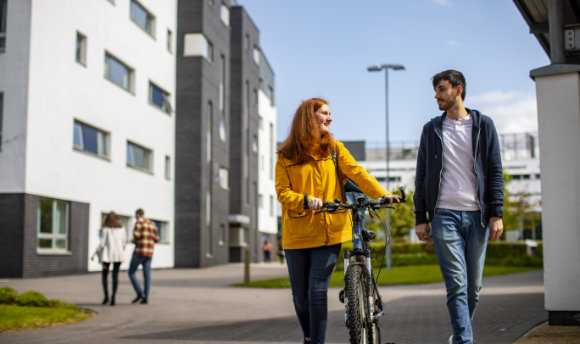 A ϲ student with a bike talking to a fellow student on campus, Edinburgh