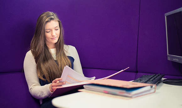 A ϲ student reading over their work against a purple wall