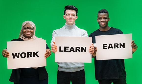 Three ϲ students holding signs with the words "Work", "Learn" and "Earn"