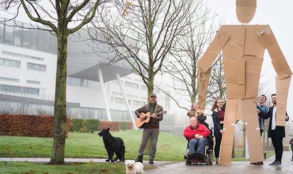 Students outside ϲ holding a giant card board person up whilst a man with a dog plays guitar