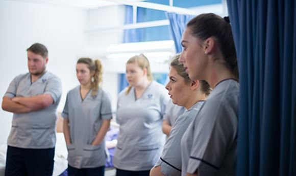A row of ϲ student nurses listening intently as a senior nurse speaks to them