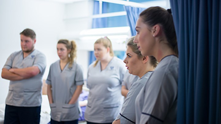 A row of ϲ student nurses listening intently as a senior nurse speaks to them