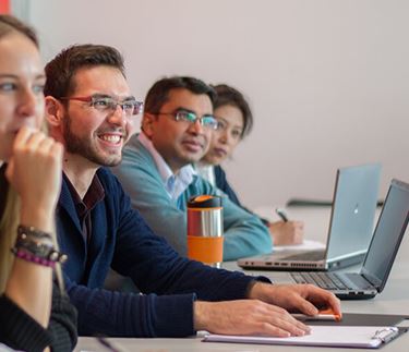 ϲ International Management with Leadership students sitting in class smiling with laptops or pads of paper and pens infront of them